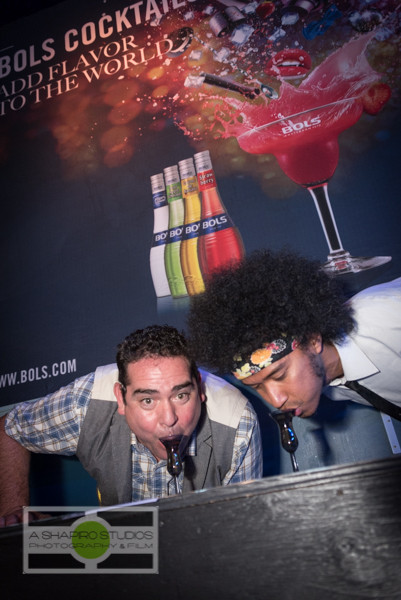 Local Bols Genever rep Jeff Schaaf shows off "Kopstootje," or Little Head-Butt - taking a drink without using your hands - with Breaks and Swells drummer Derrick Jones.  Seattle Event Photography ©2015 Ari Shapiro - AShapiroStudios.com